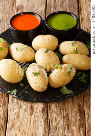 Papas arrugadas wrinkly potatoes is a traditional boiled potato dish served with a mojo rojo and mojo verde sauces close up in the plate. Vertical 84086406