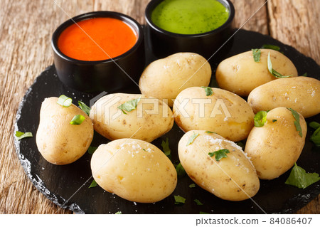 Canarian Wrinkly Potatoes Papas Arrugadas with a mojo rojo and mojo verde sauces close up in the plate. Horizontal 84086407