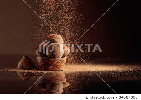 Chocolate truffles in small wooden dish sprinkled with cocoa powder. Black reflective background. Chocolate truffles in small wooden dish sprinkled with cocoa powder. Black reflective background. 84087063