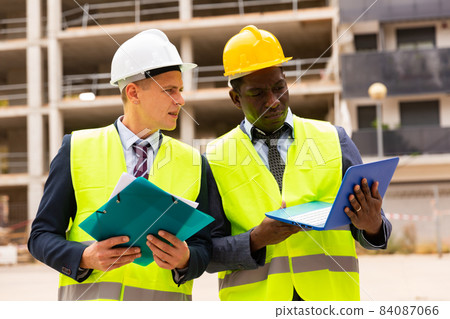 Head of construction and representative of developer are discussing documents and drawings at construction site Head of construction and representative of developer are discussing documents and drawings at construction site 84087066