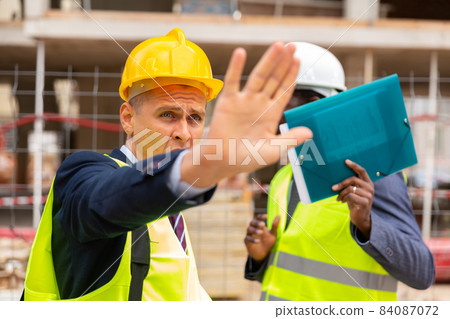 Young engineer shows a stop sign with his hand about the termination of some action Young engineer shows a stop sign with his hand about the termination of some action 84087072