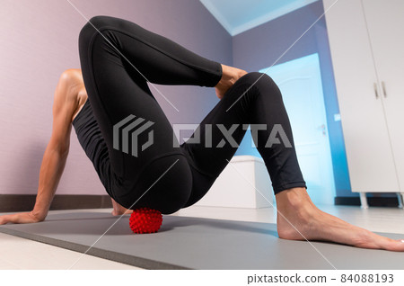 Close-up young caucasian woman doing myofascial self-massage of her thigh and buttocks with a massage ball on a massage mat. 4k resolution 84088193