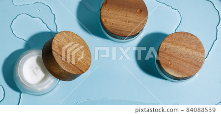 Moisture face cream in glass jar with wood lid on ocean blue wet background. Beauty, spa, wellness zero waste concept Moisture face cream in glass jar with wood lid on ocean blue wet background. Beauty, spa, wellness zero waste concept 84088539