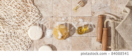 Zero waste bathroom accessories - soap, dry shampoo, exfoliating body strap, natural sea sponge with organic soap foam, wood brush, skin oil, mesh bag on earth toned stone tales top view direct 84088541