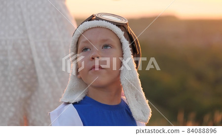 boy in hard hat close-up of face, play pilot at sunset, happy family, play childhood dream flying, kid wants to be pilot, little child on vacation travel, outdoor vacation, fantasizing about airplane 84088896