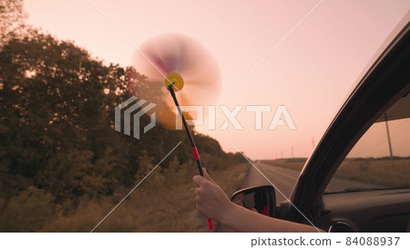 free girl waving a pinwheel out of the car window in wind, travel adventure road at pink sunset, family car ride, reach out of car window in sunlight of sky, enjoy movement, childhood dream concept free girl waving a pinwheel out of the car window in wind, travel adventure road at pink sunset, family car ride, reach out of car window in sunlight of sky, enjoy movement, childhood dream concept 84088937