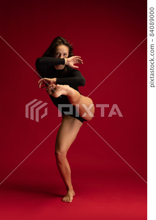 Front camera view of young emotive girl, beautiful contemp female dancer moves dynamicly isolated on dark red background. Front camera view of young emotive girl, beautiful contemp female dancer moves dynamicly isolated on dark red background. 84089000