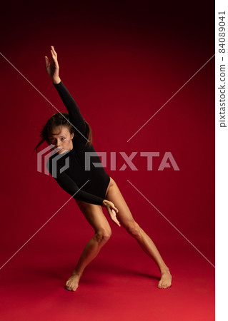 Dynamic portrait of young flexible contemp dancer dancing isolated on dark red background. Art, beauty, inspiration concept. Dynamic portrait of young flexible contemp dancer dancing isolated on dark red background. Art, beauty, inspiration concept. 84089041