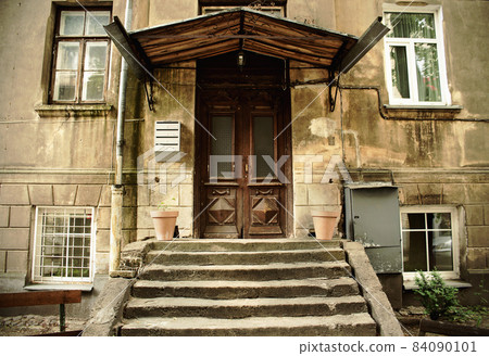 Old weathered brown entrance door under a hood with stairs Old weathered brown entrance door under a hood with stairs 84090101