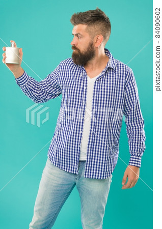 trendy caucasian guy with beard and mustache presenting male perfume on blue background, smell 84090602