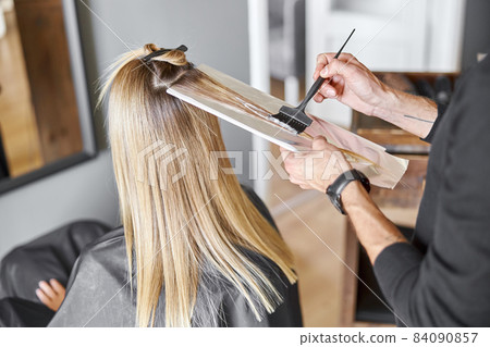 Confident male stylist is dyeing hair of blond caucasian female client Confident male stylist is dyeing hair of blond caucasian female client 84090857