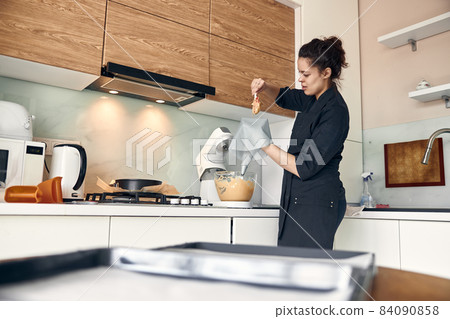 beautiful caucasian lady cook is making eclairs with help of pastry casing at home beautiful caucasian lady cook is making eclairs with help of pastry casing at home 84090858
