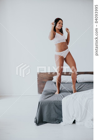 beautiful woman in lingerie dancing music in headphones on the bed in the bedroom 84093995