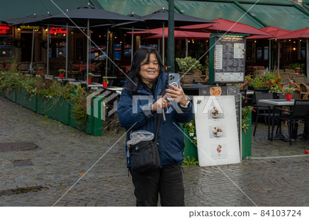 An Asian woman takes a selfie in front of a restaurant. Picture from the market square, Grote Markt, in Bruges, Belgium. 84103724