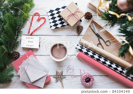 Getting ready for Christmas or New Year holiday. Flat-lay of decorations, ribbons, gift paper, door wreath, glittering balls, candy canes and cocoa with marshmallow ,top view. Christmas festive mood. Getting ready for Christmas or New Year holiday. Flat-lay of decorations, ribbons, gift paper, door wreath, glittering balls, candy canes and cocoa with marshmallow ,top view. Christmas festive mood. 84104149