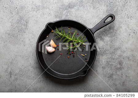 Black cast iron frying pan with rosemary, garlic, pepper top view 84105299