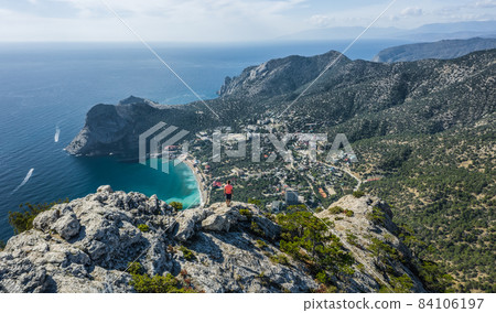 Man traveller at the top of Falcon Sokol mountain enjoying Novyi Svit town below. Crimea 84106197