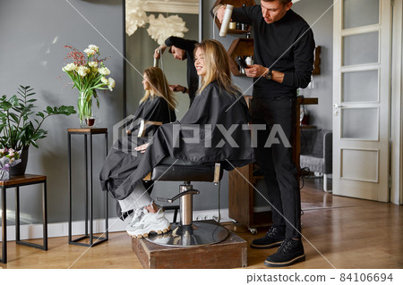 Happy beautiful light hair caucasian woman at beauty salon. Male master is drying her hair Happy beautiful light hair caucasian woman at beauty salon. Male master is drying her hair 84106694