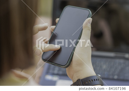 Asian woman's hand holding a smartphone and finger touching the blank screen. Sit outside with natural light. Asian woman's hand holding a smartphone and finger touching the blank screen. Sit outside with natural light. 84107196