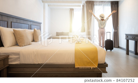 Rear view of young tourist woman raised her hands while looking to view outside window in hotel bedroom after check-in. Conceptual of travel and vacation lifestyle. Rear view of young tourist woman raised her hands while looking to view outside window in hotel bedroom after check-in. Conceptual of travel and vacation lifestyle. 84107252