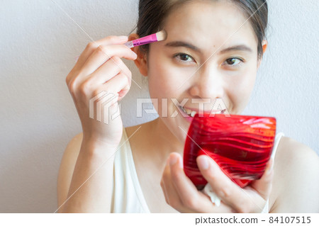 Portrait of happiness Asian woman applying concealer on her facial skin with brush. Concealer is a type of cosmetic that is used to mask dark circles, age spots, large pores etc. Portrait of happiness Asian woman applying concealer on her facial skin with brush. Concealer is a type of cosmetic that is used to mask dark circles, age spots, large pores etc. 84107515