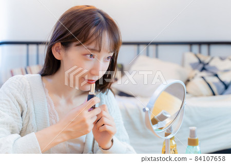 A woman who applies lipstick to her lower lip A woman who applies lipstick to her lower lip 84107658