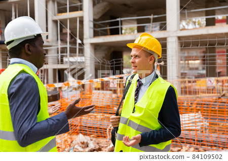 Two engineers standing on construction site and talking Two engineers standing on construction site and talking 84109502