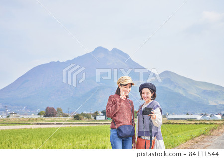 A young woman and a friend taking a commemorative photo with Mt. Yufu in the background on a girls' trip 84111544