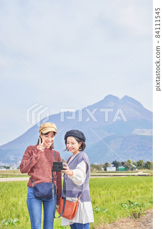 一位年輕女子和一位朋友在女孩旅行中以由布山為背景拍攝紀念照片 一位年輕女子和一位朋友在女孩旅行中以由布山為背景拍攝紀念照片 84111545