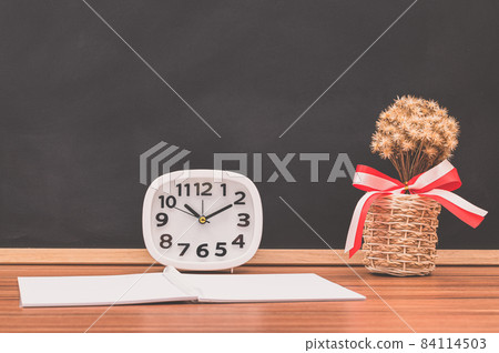 The notebook and the clock are on the table. The notebook and the clock are on the table. 84114503