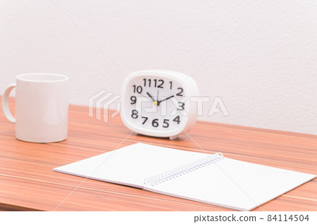 The notebook and the clock are on the table. The notebook and the clock are on the table. 84114504