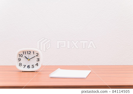 The notebook and the clock are on the table. 84114505