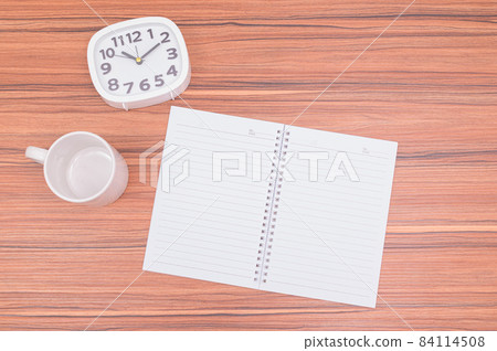 The notebook and the clock are on the table. The notebook and the clock are on the table. 84114508