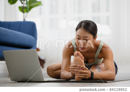 In the morning, an Asian woman is studying online yoga class, standing forward bend exercise, head to knees, uttanasana stance. In the morning, an Asian woman is studying online yoga class, standing forward bend exercise, head to knees, uttanasana stance. 84119952