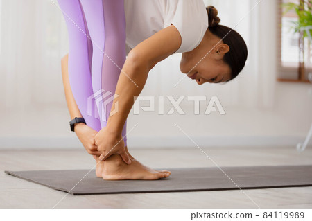 Close up hand,Asian woman is doing yoga, standing forward bend exercise, head to knees, uttanasana stance, working out, and wearing sportswear. 84119989