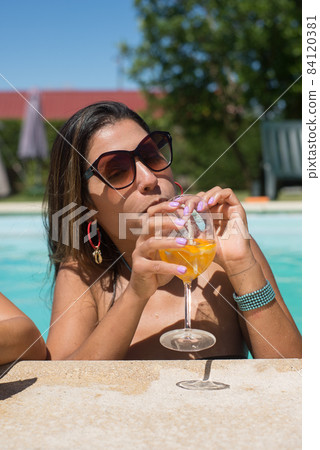 Pretty woman drinking bright cocktail in pool 84120381