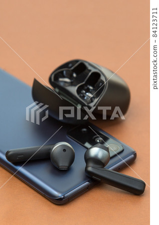 Wireless headphones are on the phone screen on a brown background, the concept of a new purchase Wireless headphones are on the phone screen on a brown background, the concept of a new purchase 84123711