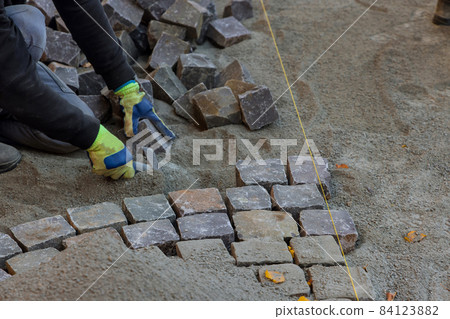 The road master in gloves lays paving stones in layers stone road by professional paver worker 84123882