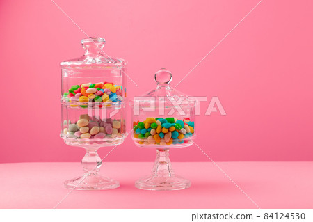 Glass containers with candies against pink background 84124530