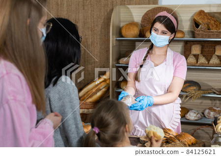 A saleswoman in a protective mask serves bought bread by two teenagers and a five-year-old sister. Sales during the ongoing COVID-19 pandemic. A saleswoman in a protective mask serves bought bread by two teenagers and a five-year-old sister. Sales during the ongoing COVID-19 pandemic. 84125621