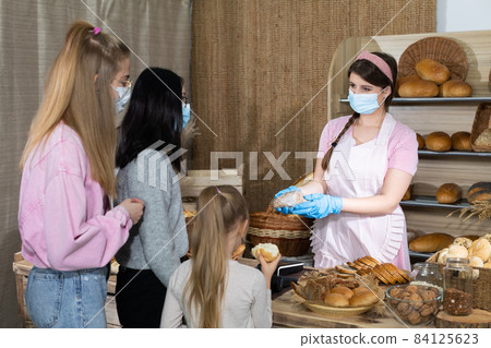 A saleswoman in a protective mask serves bought bread by two teenagers and a five-year-old sister. Sales during the ongoing COVID-19 pandemic. A saleswoman in a protective mask serves bought bread by two teenagers and a five-year-old sister. Sales during the ongoing COVID-19 pandemic. 84125623