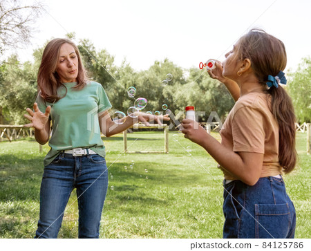Mother and daughter blowing soap bubbles in a park Mother and daughter blowing soap bubbles in a park 84125786