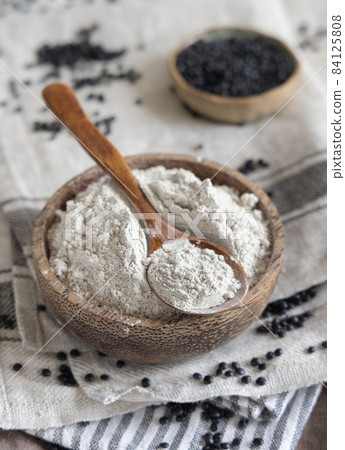 Bowl with a spoon of black lentils flour and beans on white wooden table close up 84125808