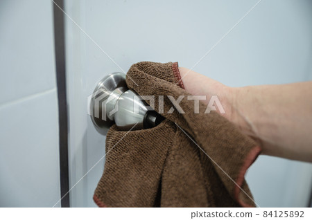 Wiping doorknob with microfiber cloth in bathroom Wiping doorknob with microfiber cloth in bathroom 84125892