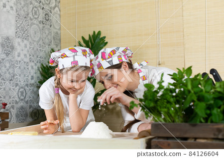 Mom tells and shows her daughter how delicate the flour is after it is sifted through a sieve. Kitchen experiences with flour in the family circle. Mom tells and shows her daughter how delicate the flour is after it is sifted through a sieve. Kitchen experiences with flour in the family circle. 84126604