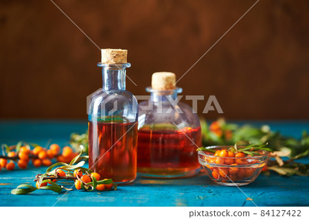 Glass bottle with sea buckthorn oil berries and sea buckthorn branches on wooden background Glass bottle with sea buckthorn oil berries and sea buckthorn branches on wooden background 84127422