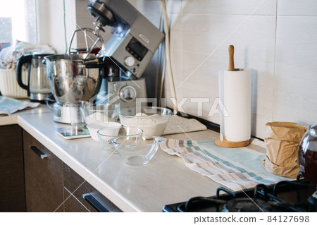 Products and ingredients on kitchen table ready for making Christmas gingerbread. Lifestyle still life Making Christmas gingerbread at home. Ingredients, bakeware, dough rolling pin and utensils 84127698