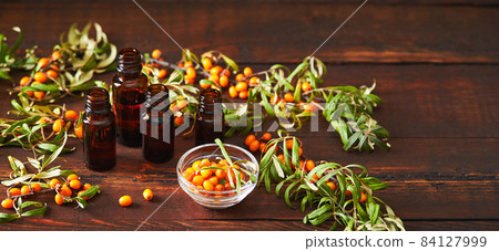 Glass bottle with sea buckthorn oil berries and sea buckthorn branches on wooden background Glass bottle with sea buckthorn oil berries and sea buckthorn branches on wooden background 84127999