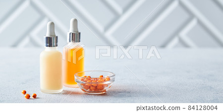 Glass bottles with seabackthorn face or body skin care products on light background. Self-care, cosmetics, beauty practices, self-care concept 84128004