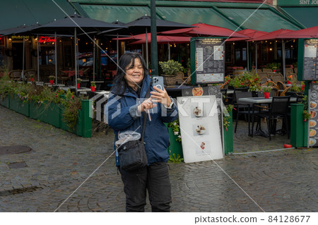 An Asian woman takes a selfie in front of a restaurant. Picture from the market square, Grote Markt, in Bruges, Belgium. 84128677